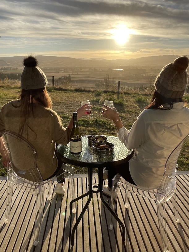 Two Women Sittin on deck, drinking wine, overlooking vineyards
