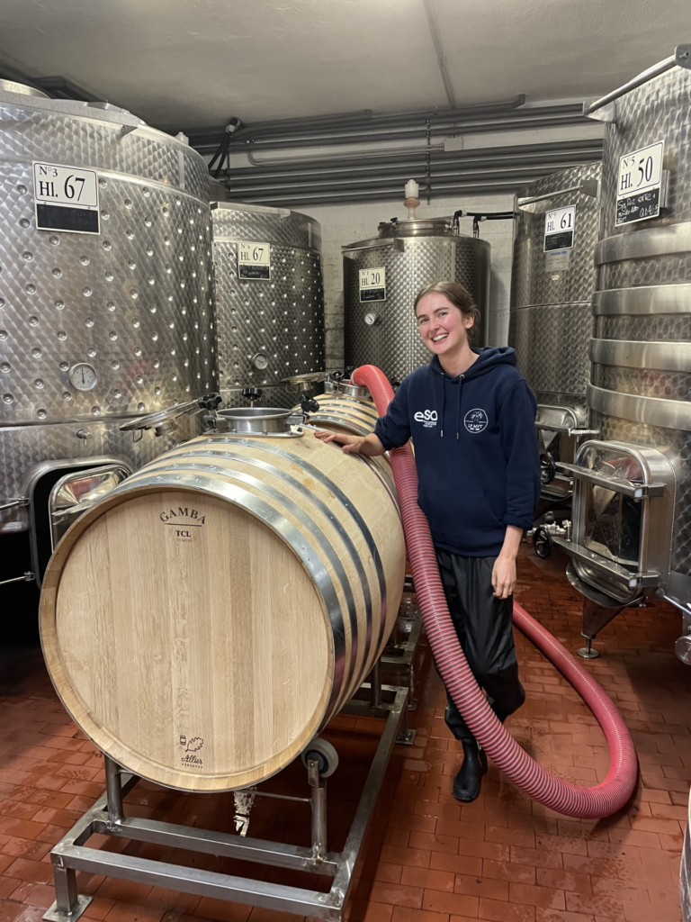 Female vintage staff standing with oak barrel and tanks.